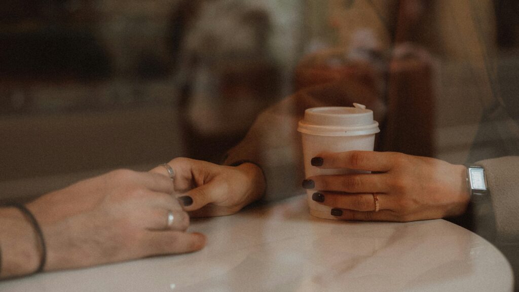 Close-up of hands holding coffee cups at a cafe, capturing a warm and intimate moment.