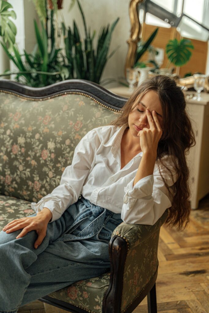 A woman relaxes on a floral vintage sofa in a cozy, light-filled room with plants.